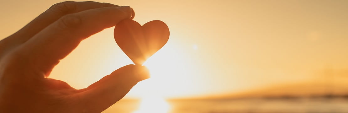 A hand holding heart against a beautiful sunset.
