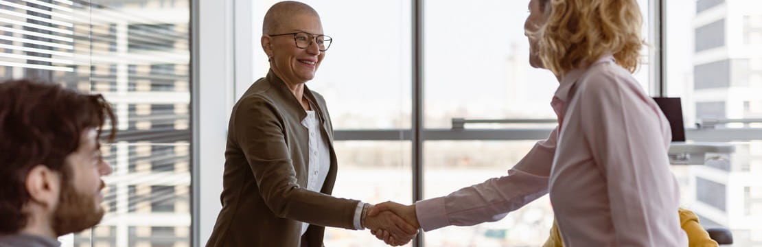 Businesswomen standing and shaking hands across a conference table.